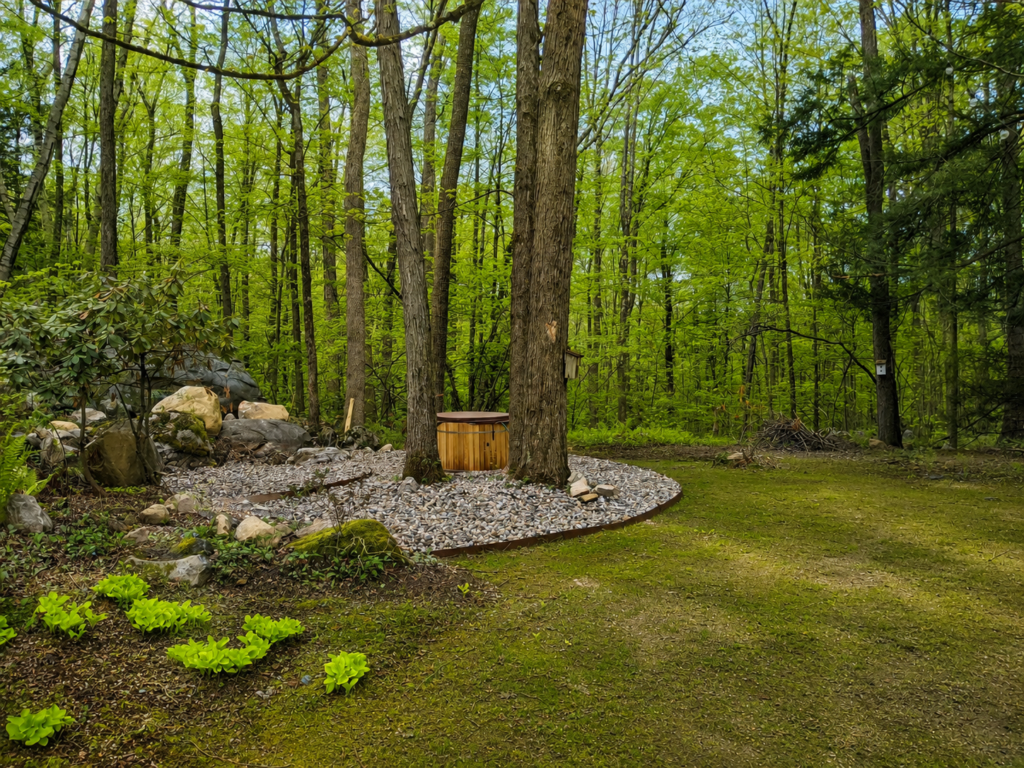 Completed Berkshire Rock Garden with river rock, curved steel edging and a cedar hot tub among mature woodland trees