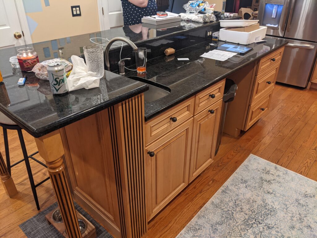 Original two-level kitchen island with natural wood cabinets and dark countertops before remodeling