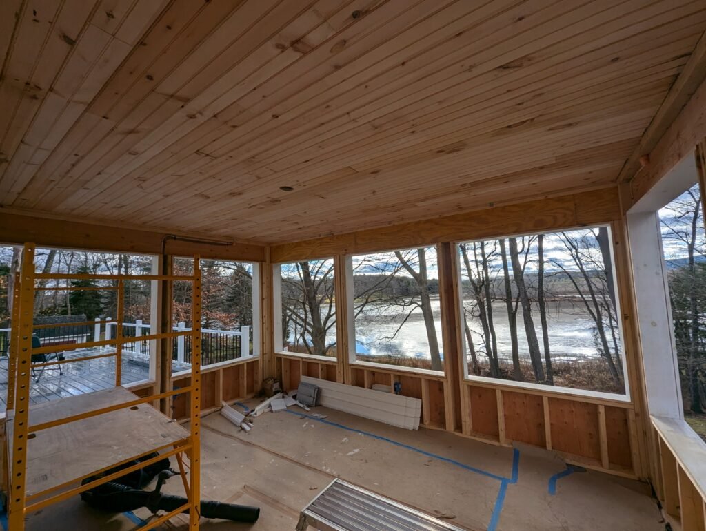 Three-season room under construction with large window openings, a V-board ceiling and views of Pontoosuc Lake