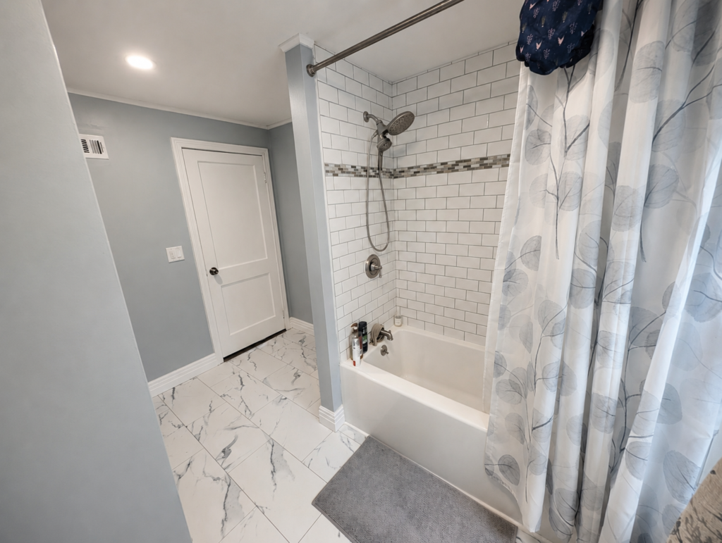 New bathtub with a white subway-tile surround, mosaic accent and marble-look bathroom flooring
