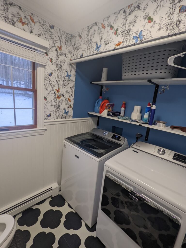 Completed laundry area with blue walls, white beadboard, open shelving and black-and-white epoxy flooring