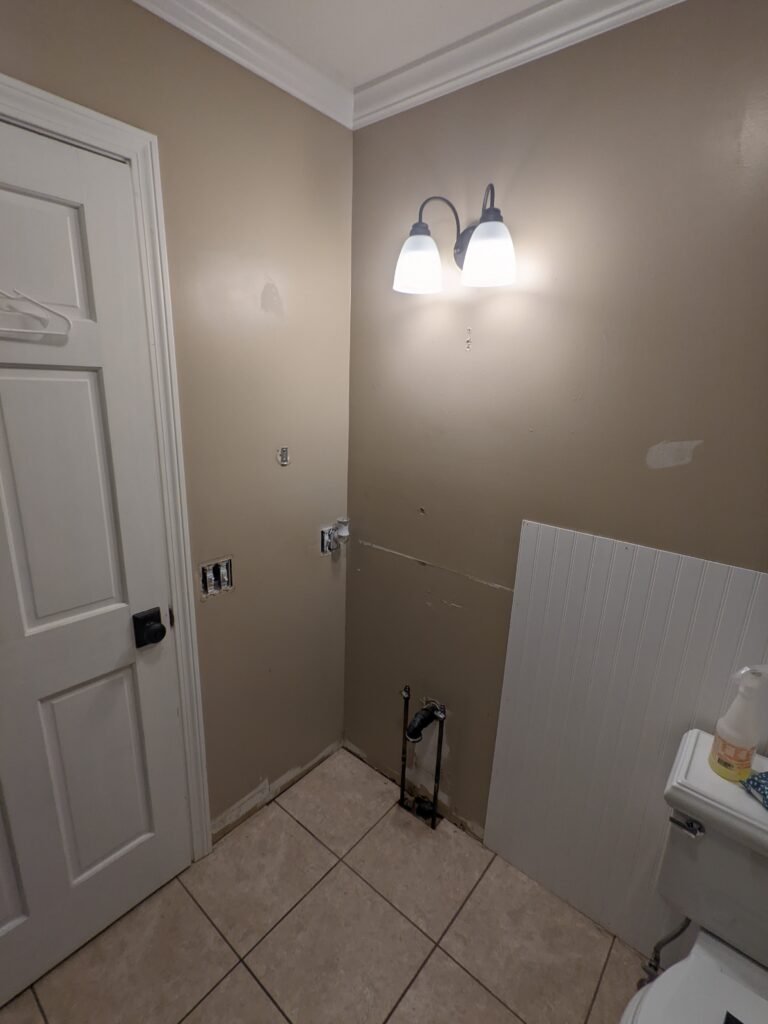 Combined bathroom and laundry room before remodeling with open shelving above the washer and dryer