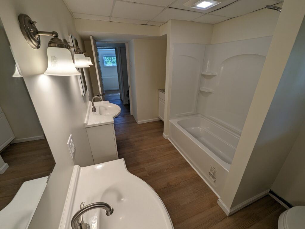 Completed bathroom in the Lower House apartment with a tub-shower, vanity and durable flooring