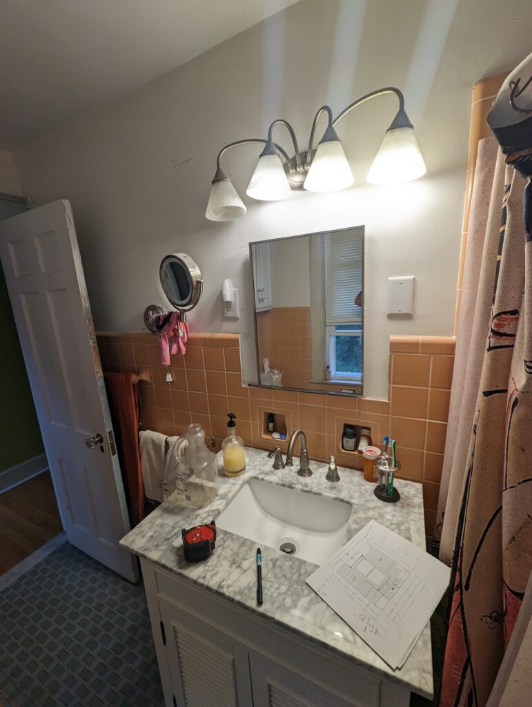 Original bathroom vanity, mirror and peach wall tile before the complete renovation