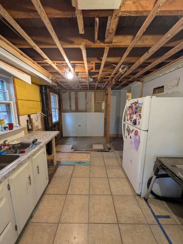 Galley kitchen before renovation with aging white cabinets, tile flooring and the original refrigerator location