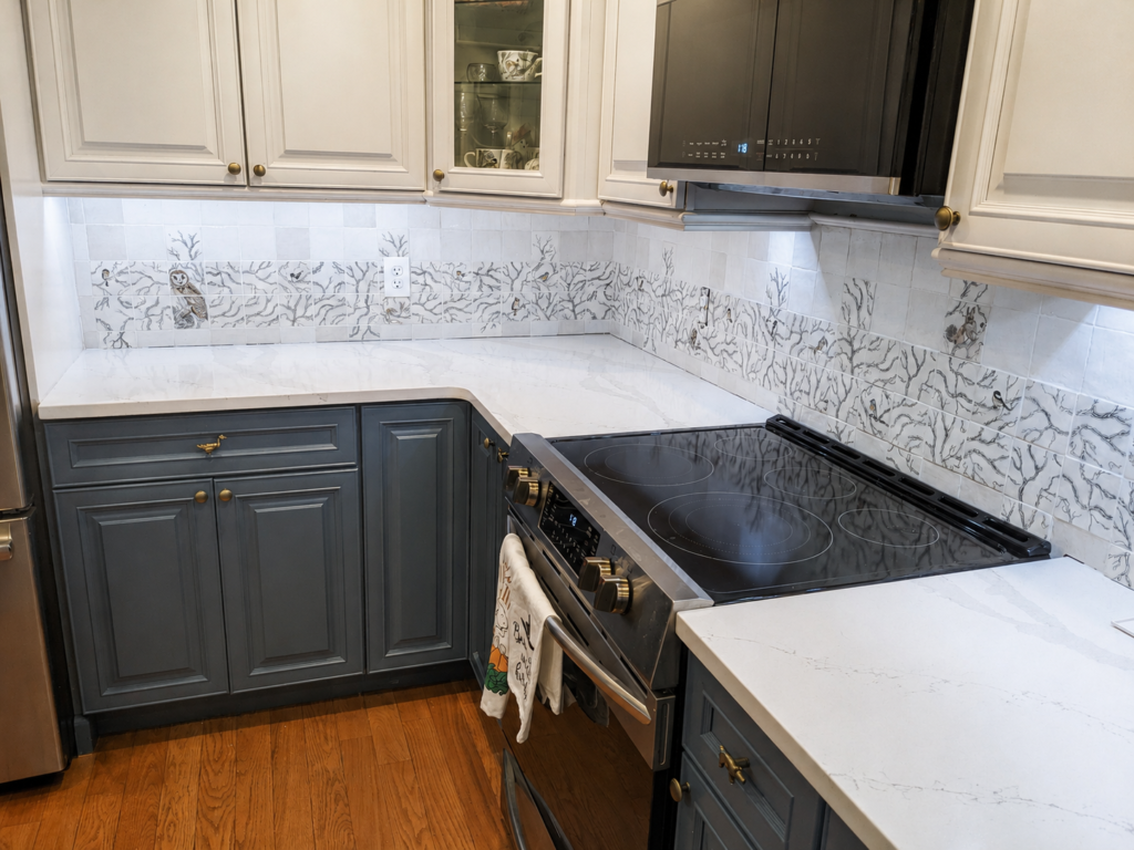 Completed hand-painted woodland backsplash with illustrated branches, birds and an owl behind the kitchen range