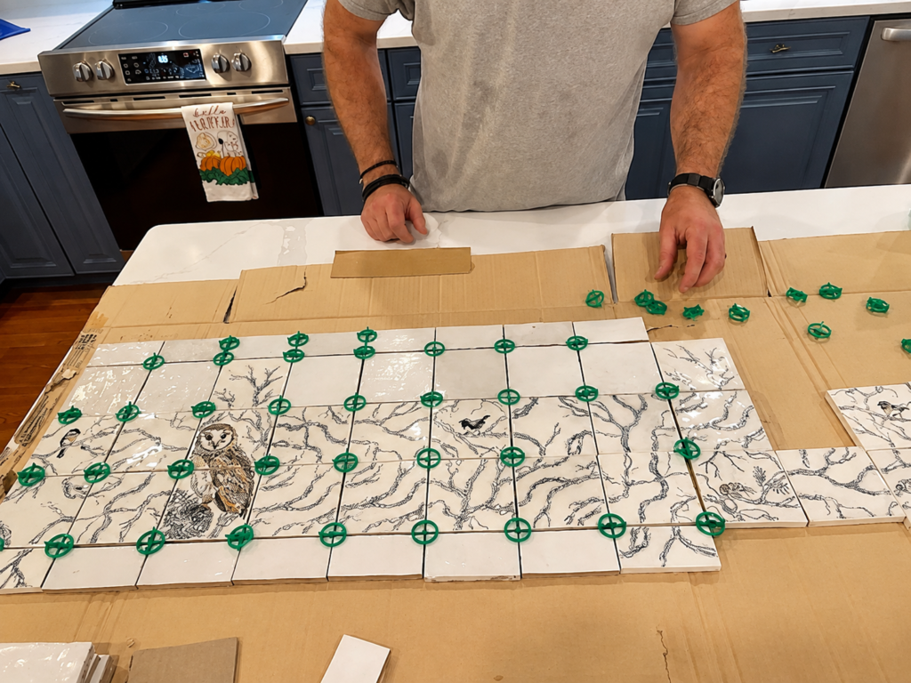 Hand-painted woodland backsplash tiles dry-laid before installation to organize the continuous owl and branch design
