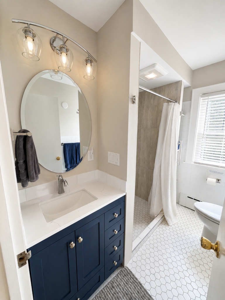 Completed Modern Classic Bath with a navy vanity, light-veined countertop, walk-in shower and white hexagonal flooring