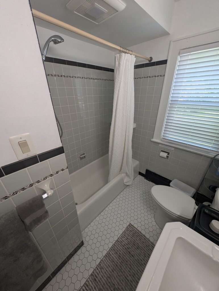 Bathroom before renovation with an original bathtub, gray wall tile, toilet and hexagonal floor