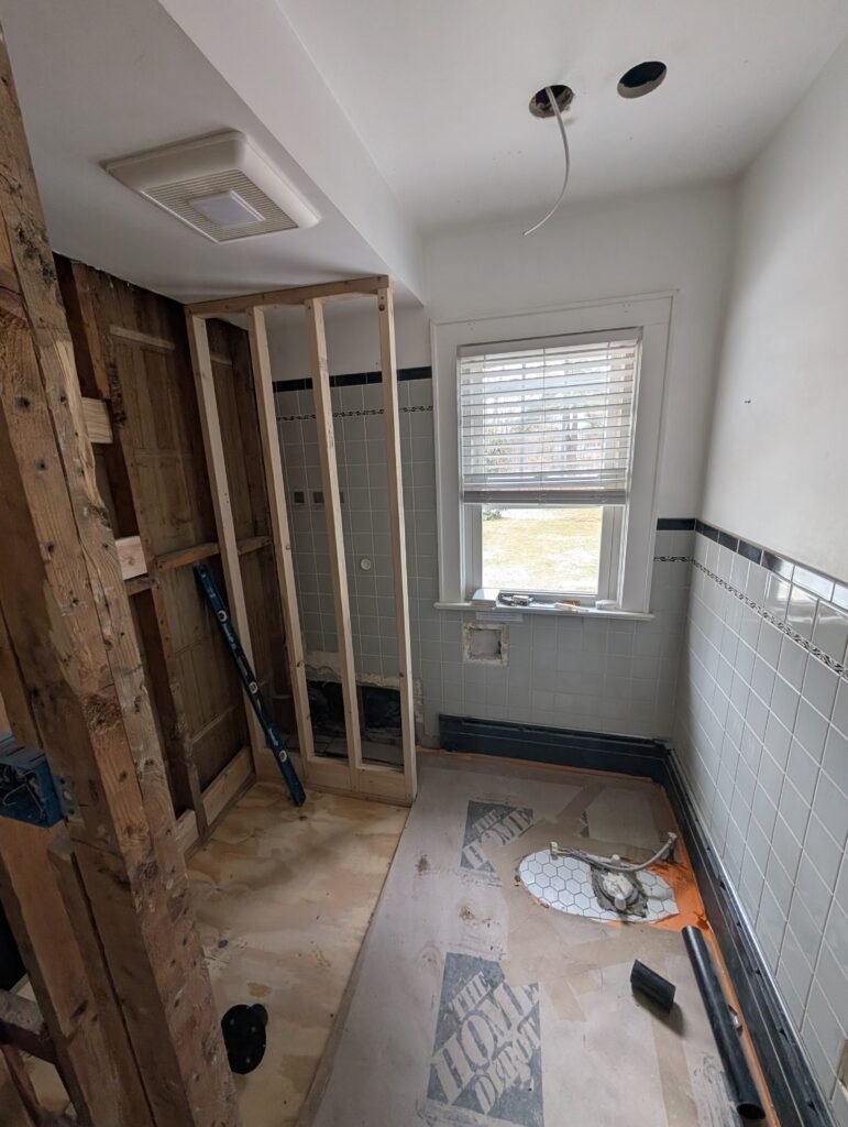 Bathroom during demolition with the bathtub removed and new shower wall framing under construction