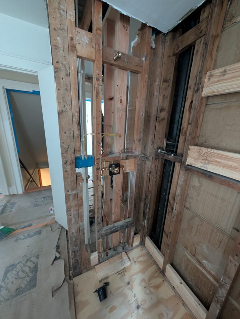 Open bathroom wall during renovation showing new plumbing and electrical work within the existing framing